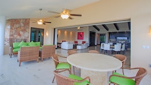 A spacious indoor area with wicker furniture, a round table, ceiling fans, and a stone wall. - Condo Gerbera in Punta Mita (Punta de Mita)