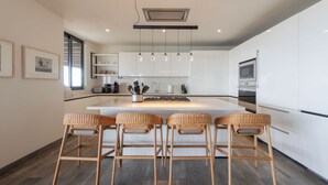Una cocina moderna con armarios blancos, una isla central con taburetes y luminarias colgantes, además de un horno empotrado.