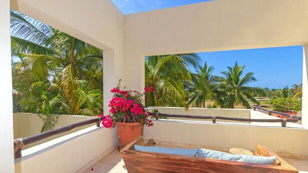 A balcony with a wooden bench, a potted plant with pink flowers, and a view of palm trees. - Condo Palma Azul in Punta Mita (Punta de Mita)
