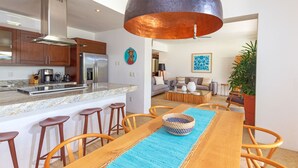 A modern kitchen with stainless steel appliances, a large copper pendant light, and a dining area with wooden chairs and a blue placemat. - Condo Palma Azul in Punta Mita (Punta de Mita)