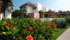 A modern building with a thatched roof, surrounded by lush greenery and vibrant flowers. - Villa Aguamarina in Punta Mita (Punta de Mita)