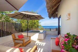 A balcony with a wooden chair, a cushioned sofa, a large umbrella, and a hot tub. - Villa Aguamarina in Punta Mita (Punta de Mita)