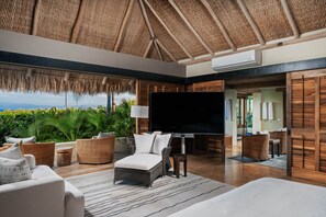 A modern outdoor living area with a thatched roof, wicker furniture, a flat-screen TV, and a view of the ocean. - Villa Aire in Punta Mita (Punta de Mita)