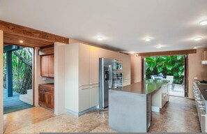 A modern kitchen with a central island, built-in appliances, and a view of lush greenery. - Villa Aire in Punta Mita (Punta de Mita)