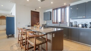 A modern kitchen with a central island, wooden chairs, and built-in appliances. - Condo Kumar in Punta Mita (Punta de Mita)