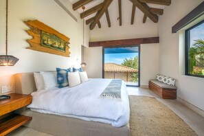 Ein Schlafzimmer mit einem großen Bett, einem Holz-Kopfteil, einer Bank am Fenster und Blick ins Freie.