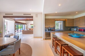 Eine moderne Küche mit Holzausstattung, einer zentralen Kochinsel mit Barhocker und einem Essbereich mit rundem Tisch und Stühlen.