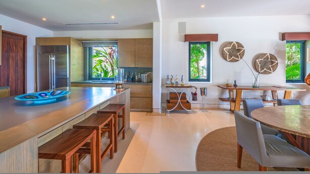 A modern kitchen with wooden countertops, a built-in refrigerator, and a dining area with a round table and chairs. - Casa Marlago in Punta Mita (Punta de Mita)