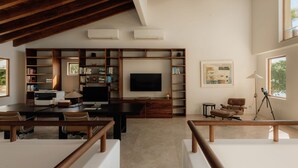 Un salon moderne doté d’un grand téléviseur à écran plat, de bibliothèques en bois, d’un bureau avec un ordinateur et d’un coin salon confortable.