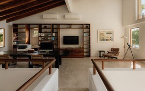 A modern living room with a large flat-screen TV, wooden bookshelves, a desk with a computer, and a comfortable seating area. - Estate Jaguar in Punta Mita (Punta de Mita)
