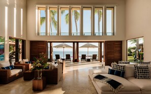 A spacious living area with a high ceiling, large windows, and a view of the ocean. - Estate Jaguar in Punta Mita (Punta de Mita)
