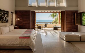 A bedroom with a bed, a nightstand, a lamp, a window with a view of the ocean, and a balcony with chairs. - Estate Jaguar in Punta Mita (Punta de Mita)