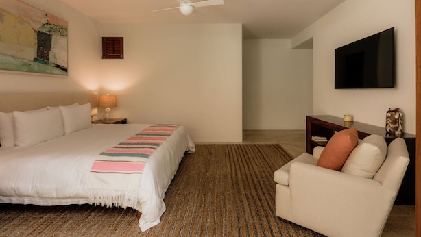 Une chambre à coucher comprenant un lit, un bureau, une chaise, un téléviseur et un ventilateur de plafond.