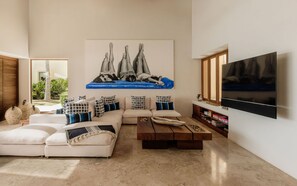 A modern living room with a sectional sofa, a coffee table, a flat-screen TV, and a large abstract painting on the wall. - Estate Jaguar in Punta Mita (Punta de Mita)