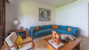 Un salon avec un canapé d’angle bleu, une table basse en bois, un fauteuil, une lampe et une œuvre d’art encadrée accrochée au mur.