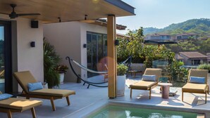 Un espace piscine avec des chaises longues, un hamac et une vue sur les maisons au loin.