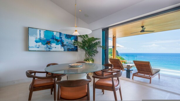 Un espace repas moderne avec une table en verre, des chaises en bois et une vue sur l’océan.
