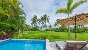 Une piscine entourée de palmiers et d’une pelouse bien entretenue, avec des chaises longues et un parasol.