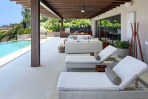 Ein überdachter Außenbereich mit Pool, Liegestühlen und Grill.