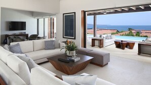 A modern living room with a large sofa, a coffee table, and a TV. There is a view of the sea through large windows. - Casa Rincon del Mar in Punta Mita (Punta de Mita)