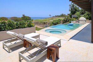 Ein Poolbereich im Freien mit Liegestühlen und Blick aufs Meer.