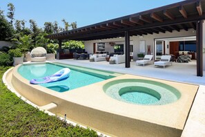 Ein moderner Poolbereich im Freien mit Whirlpool, Liegestühlen und einer überdachten Terrasse.