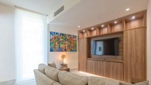 Ein Wohnzimmer mit einer Couch, einem an einer Holzkommode befestigten Fernseher, einem Bild an der Wand und einem kleinen Tisch mit einer Lampe.