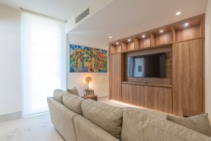 A living room with a sofa, a TV mounted on a wooden cabinet, a painting on the wall, and a small table with a lamp. - Casa Yeiya in Punta Mita (Punta de Mita)