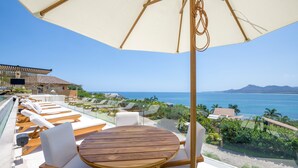 Eine Terrasse mit Holztisch und -stühlen, einem großen Sonnenschirm und Blick aufs Meer.