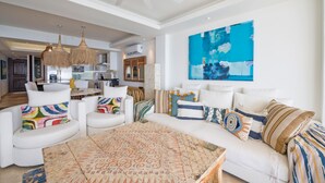 A spacious living area with a ceiling fan, a large abstract painting, and a modern kitchen in the background. - Condo Ocean in Punta Mita (Punta de Mita)