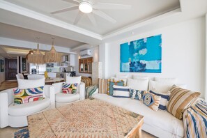 A spacious living area with a ceiling fan, a large abstract painting, and a modern kitchen in the background. - Condo Ocean in Punta Mita (Punta de Mita)
