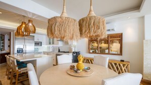A modern kitchen with white cabinets, a central island, and a dining area with a round table and white chairs. - Condo Ocean in Punta Mita (Punta de Mita)