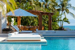 Ein Poolbereich mit Liegestühlen, einer Pergola und Blick auf den Ozean.