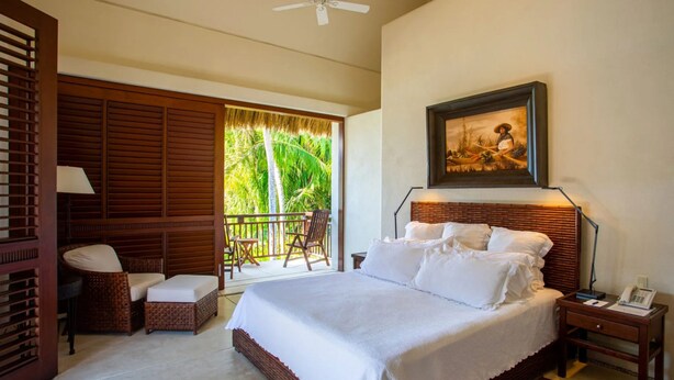 A bedroom with a large bed, a balcony with wicker furniture, a painting on the wall, and a ceiling fan. - Casa Familia in Punta Mita (Punta de Mita)