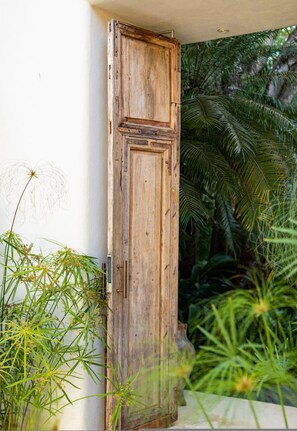 A wooden door with a rustic design, a white wall, and lush green foliage in the background. - Casa Familia in Punta Mita (Punta de Mita)