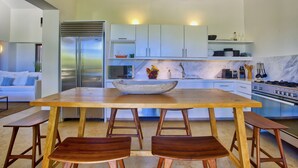 A modern kitchen with a large wooden table, two wooden benches, a stainless steel refrigerator, white cabinets, and a marble countertop. - Penthouse Pacifico in Punta Mita (Punta de Mita)