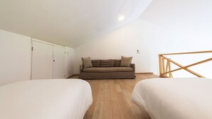 A loft-style bedroom with two beds, a sofa bed, wooden flooring, and white walls. - Penthouse Pacifico in Punta Mita (Punta de Mita)