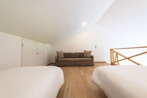 Ein Schlafzimmer im Loft-Stil mit zwei Betten, einer Schlafcouch, Holzdielen und weißen Wänden.