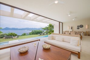 A modern living room with a large window overlooking a pool and mountains. - Estate Ikal in Punta Mita (Punta de Mita)