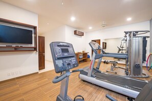 Ein Heimfitnessraum mit Laufband, Kraftgerät und Wandfernseher.
