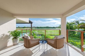 A balcony with wicker chairs, a small table, and a view of a golf course. - Condo Allegra in Punta Mita (Punta de Mita)