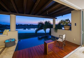 An infinity pool with a wooden deck, a chair, and a potted plant. - Condo Lago in Punta Mita (Punta de Mita)