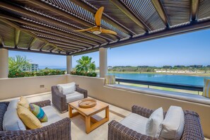 A covered outdoor seating area with wicker furniture, a ceiling fan, and a view of a body of water. - Condo Lago in Punta Mita (Punta de Mita)
