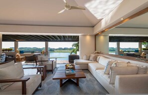 A modern living room with a large window, a ceiling fan, and a view of a body of water. - Condo Lago in Punta Mita (Punta de Mita)