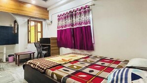A bedroom with a bed, a desk, a chair, a ceiling fan, and a window with curtains. - Hotel Sagar Bela OD (Puri)
