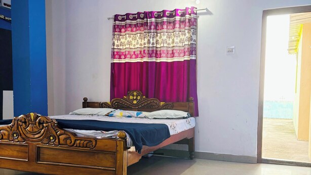 A bedroom with a wooden bed, a curtain, and a view through an open door. - Hotel Sagar Bela OD (Puri)