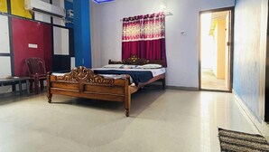 A bedroom with a bed, a ceiling fan, a window with curtains, and a door. - Hotel Sagar Bela OD (Puri)