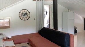 Ett rum med en soffa, en klocka, ett fönster med gardiner och en dörr.