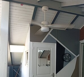 A room with a ceiling fan, a clock, and a door leading to another room. - Villa top studio (BAIE MAHAULT)