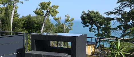 Ein Balkon mit einem Korbstuhl-Set, einem Blumentopf und Blick auf das Meer.